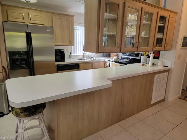 Kitchen with a peninsula, glass insert cabinets, stainless steel appliances, and light countertops