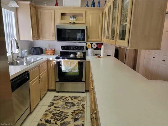 Kitchen featuring light brown cabinets, a sink, light countertops, appliances with stainless steel finishes, and glass insert cabinets