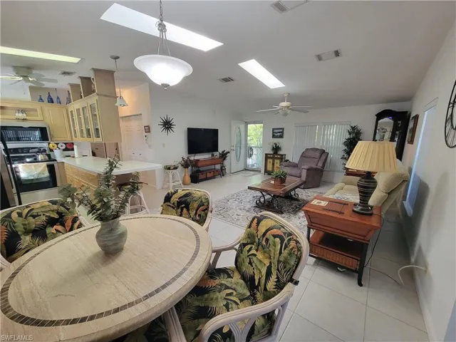 Living room featuring light tile patterned floors, vaulted ceiling with skylight, ceiling fan, and visible vents