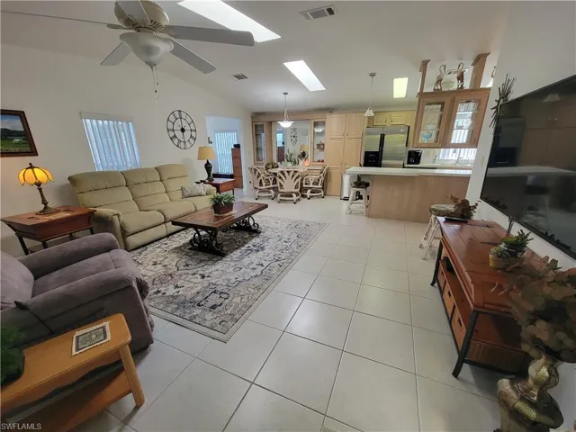 Living room featuring lofted ceiling with skylight, visible vents, a ceiling fan, and light tile patterned flooring