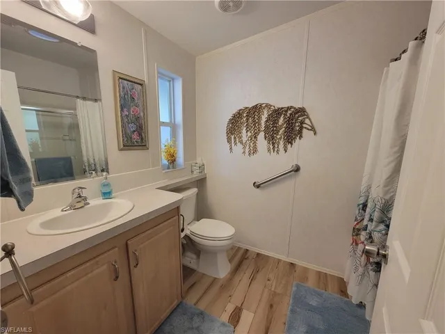 Bathroom featuring curtained shower, visible vents, toilet, vanity, and wood finished floors
