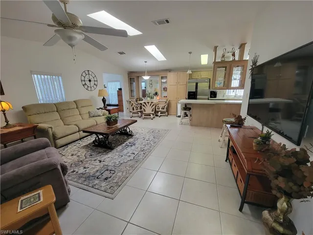 Living area featuring a ceiling fan, vaulted ceiling with skylight, visible vents, and light tile patterned flooring