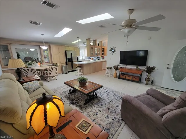 Living area with light tile patterned floors, lofted ceiling with skylight, and visible vents