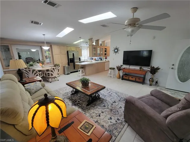 Living area featuring light tile patterned floors, vaulted ceiling with skylight, ceiling fan, and visible vents