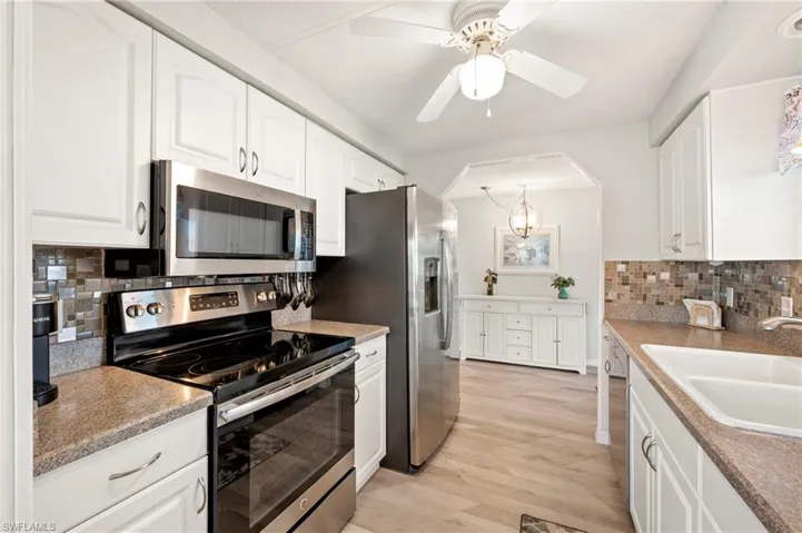 Kitchen featuring appliances with stainless steel finishes, a sink, tasteful backsplash, and white cabinets