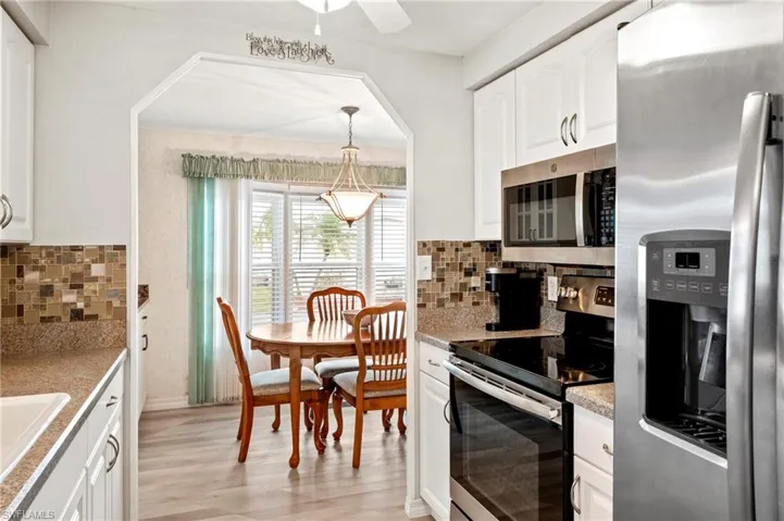 Kitchen with appliances with stainless steel finishes, light wood-style flooring, decorative backsplash, and white cabinetry