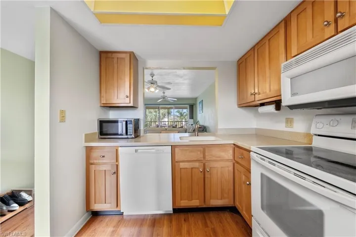 Kitchen with white appliances, light wood-type flooring, light countertops, ceiling fan, and brown cabinetry