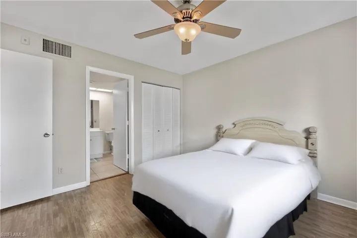 Bedroom with wood finished floors, a closet, ensuite bath, and a ceiling fan
