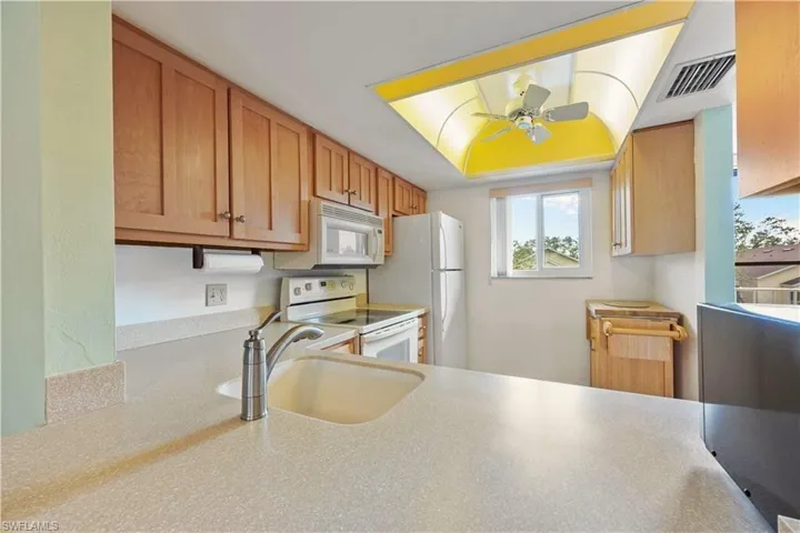 Kitchen featuring white appliances, ceiling fan, light countertops, and brown cabinetry