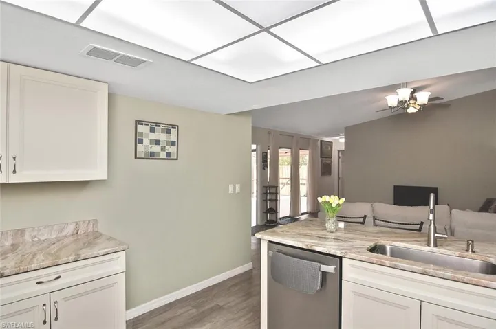 Kitchen featuring white cabinetry, stainless steel dishwasher, light stone countertops, dark wood-style floors, and open floor plan