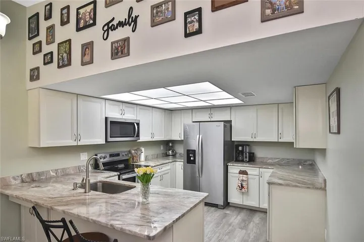 Kitchen with stainless steel appliances, light stone counters, a breakfast bar, white cabinetry, and a peninsula