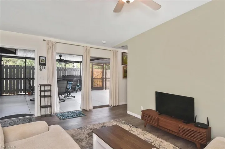 Living room featuring a ceiling fan, dark wood-type flooring, and a sunroom