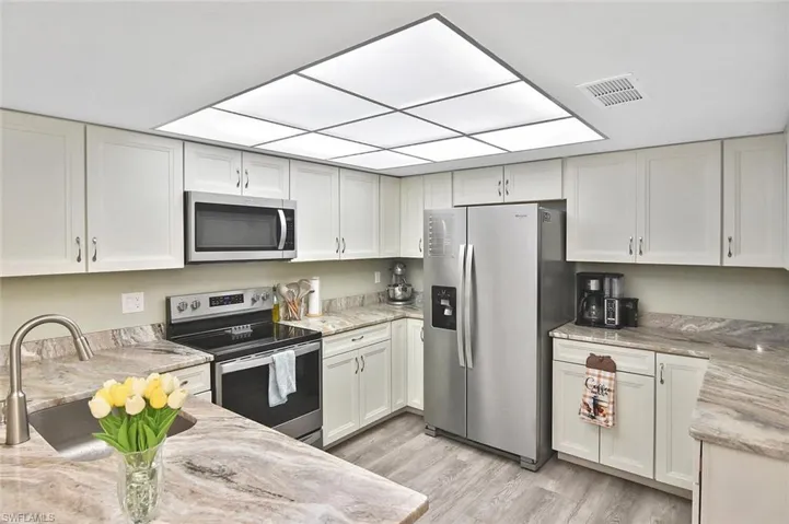 Kitchen featuring appliances with stainless steel finishes, light stone countertops, light wood-type flooring, and white cabinetry