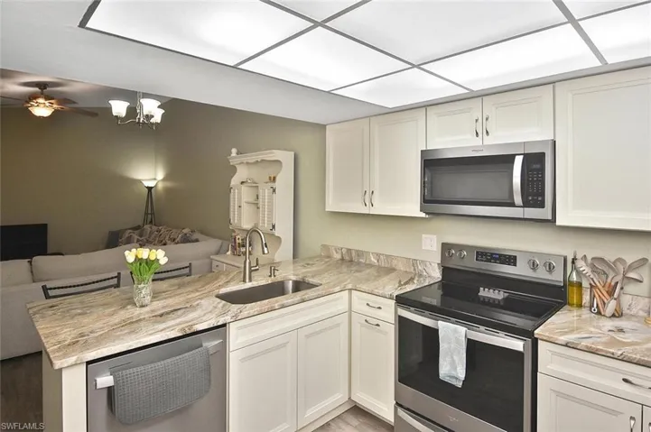 Kitchen featuring a peninsula, stainless steel appliances, open floor plan, light stone countertops, and white cabinets