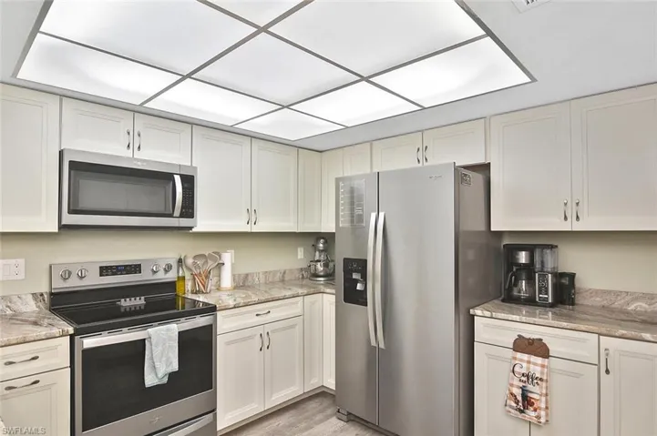 Kitchen with appliances with stainless steel finishes, light stone counters, light wood-type flooring, and white cabinetry