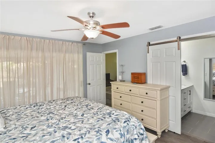 Bedroom with a barn door, dark wood-style flooring, and a ceiling fan