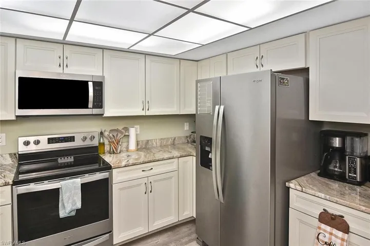 Kitchen with appliances with stainless steel finishes, light stone countertops, and white cabinetry