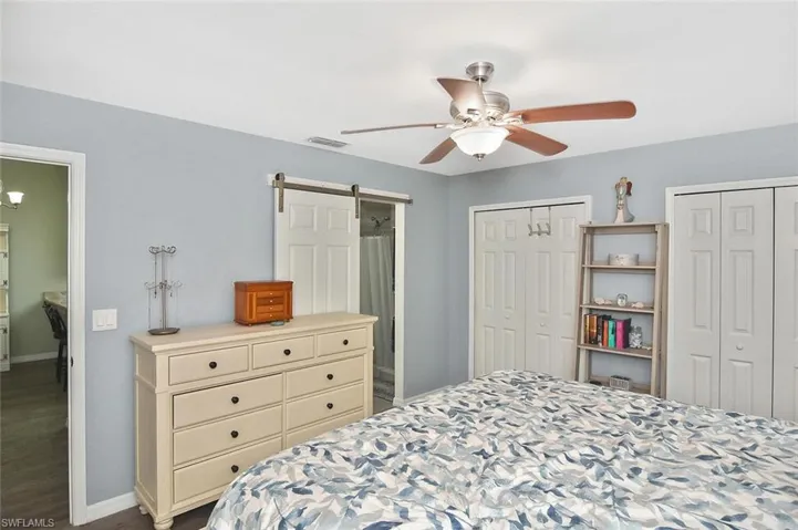 Bedroom featuring multiple closets, ceiling fan, a barn door, and dark wood-style floors