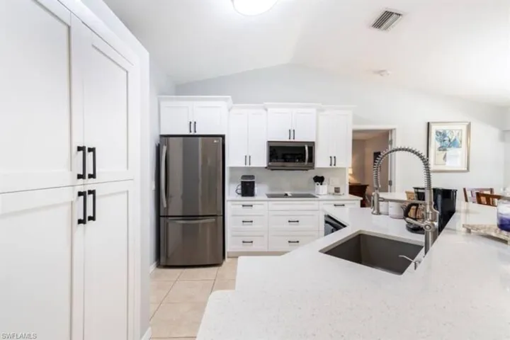 Kitchen featuring white cabinets, stainless steel appliances, vaulted ceiling, and sink
