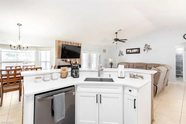 Kitchen featuring stainless steel dishwasher, ceiling fan with notable chandelier, lofted ceiling, and a healthy amount of sunlight