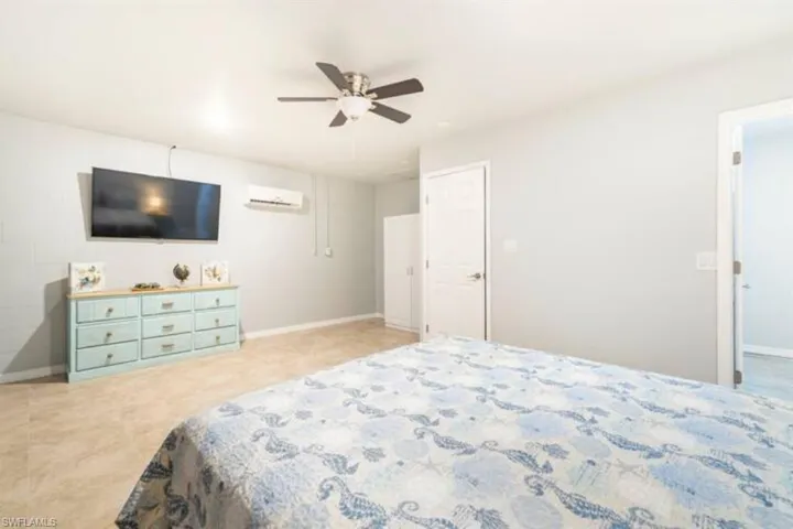 Tiled bedroom with a wall mounted AC and ceiling fan