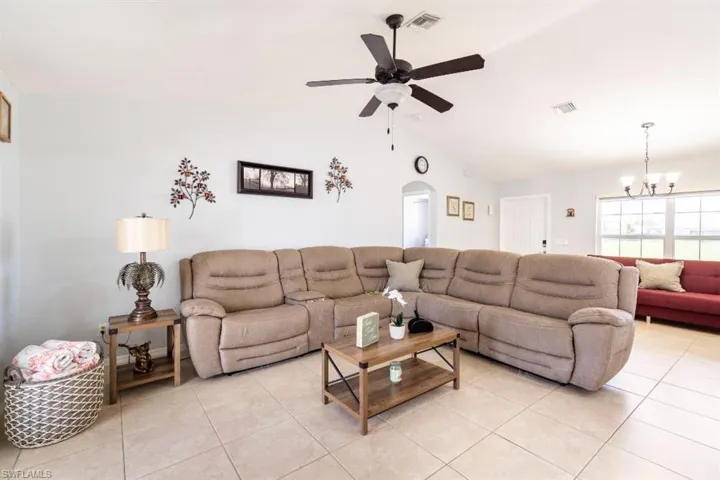 Living room with lofted ceiling, ceiling fan with notable chandelier, and light tile patterned floors