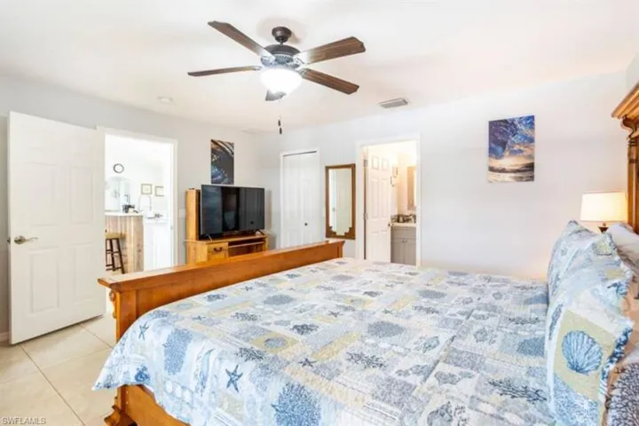 Bedroom featuring a closet, ensuite bathroom, light tile patterned floors, and ceiling fan
