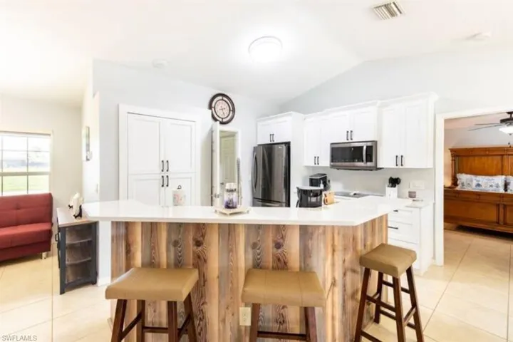 Kitchen with ceiling fan, stainless steel appliances, lofted ceiling, light tile patterned floors, and a kitchen breakfast bar