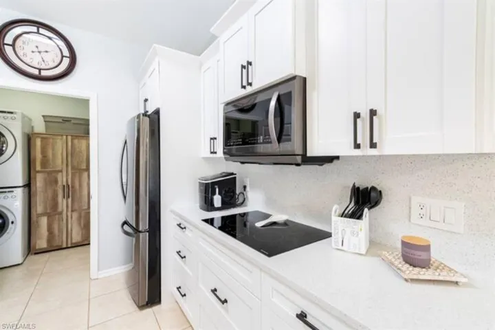 Kitchen with white cabinetry, tasteful backsplash, stainless steel appliances, stacked washing maching and dryer, and light tile patterned floors