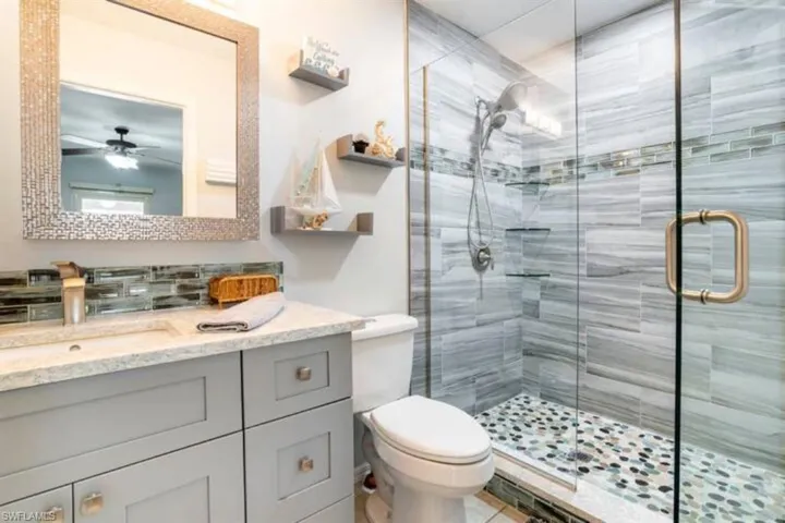 Bathroom featuring a shower with shower door, vanity, ceiling fan, and toilet