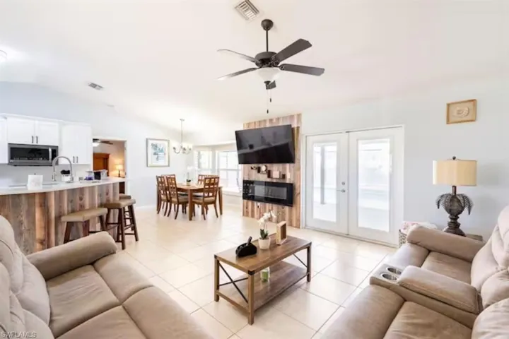 Living room featuring sink, french doors, ceiling fan with notable chandelier, lofted ceiling, and light tile patterned flooring