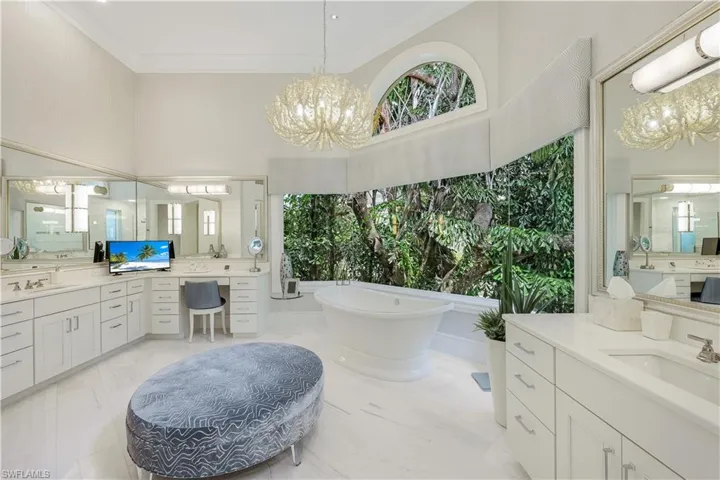 Relax in this spa-inspired primary bath with his/her vanities, a separate makeup area, a soaking tub, and an oversized walk-in shower overlooking lush, tropical greenery.
