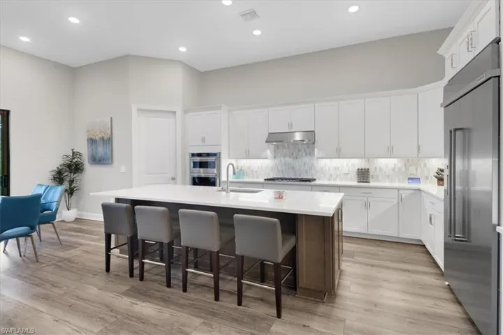 Kitchen featuring appliances with stainless steel finishes, white cabinetry, light wood-type flooring, and an island with sink