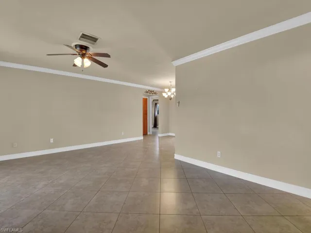 Empty room featuring suspended lighting, ceiling fan, ornamental molding, and light tile patterned flooring