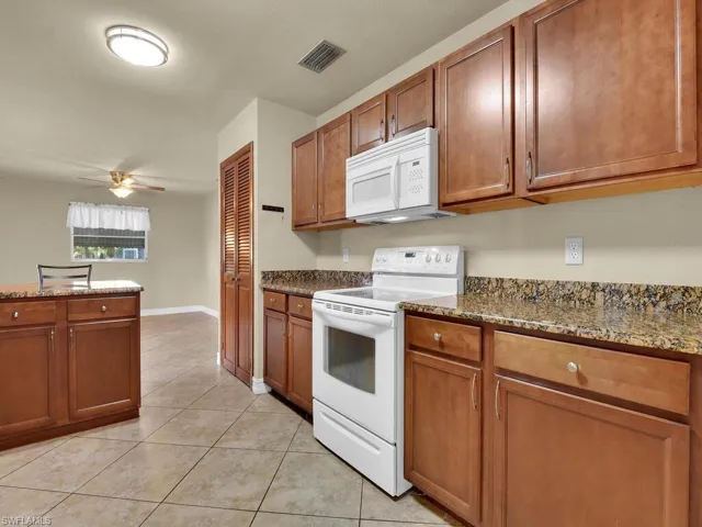 Kitchen with white appliances, dark stone counters, and wood finish cabinets