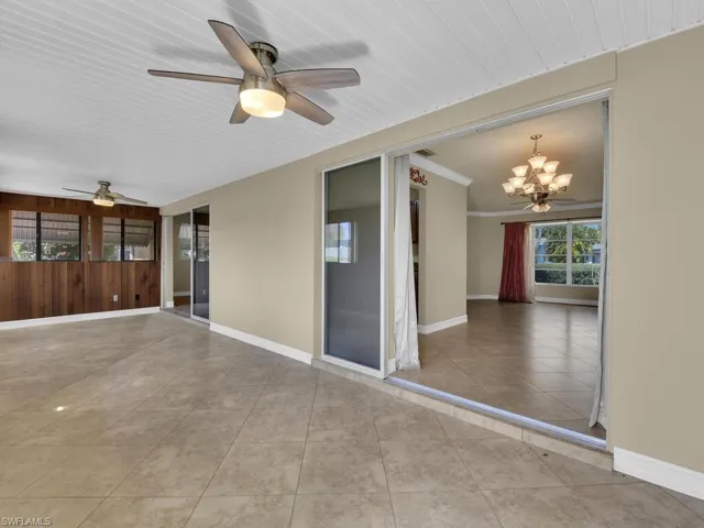 Unfurnished room featuring ceiling fan, healthy amount of natural light, a chandelier, wood walls, and light tile patterned floors