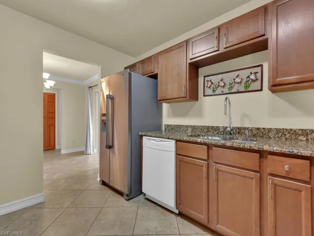 Kitchen with dark stone counters, dishwasher, high end refrigerator, crown molding, and wood finish cabinets