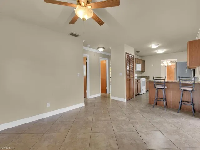 Kitchen with white appliances, wood finish cabinetry, crown molding, suspended lighting, and light stone countertops