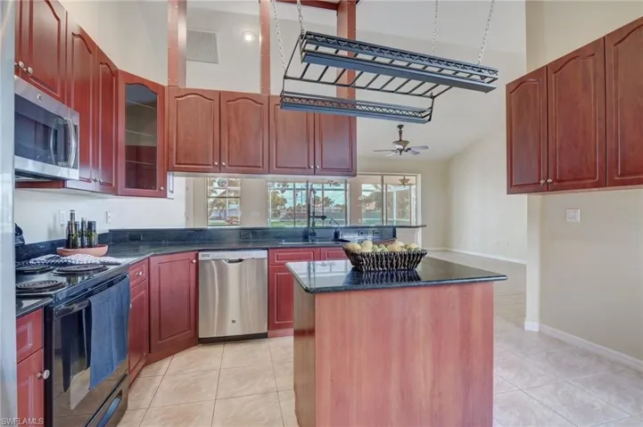 Kitchen with dark stone counters, light tile patterned flooring, ceiling fan, stainless steel appliances, and a center island
