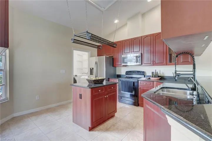 Kitchen with a high ceiling, dark stone counters, stainless steel appliances, and light tile patterned floors