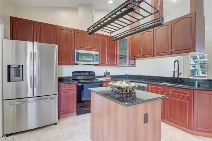 Kitchen with sink, dark stone countertops, a kitchen island, appliances with stainless steel finishes, and light tile patterned floors
