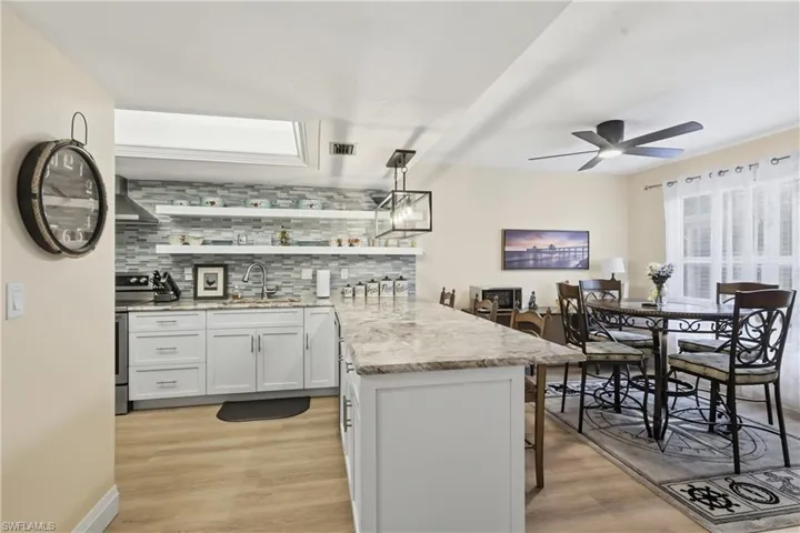 Kitchen featuring white cabinetry, a tiled backsplash, wood-finish flooring, a kitchen island with a stone countertop, and an adjacent dining area