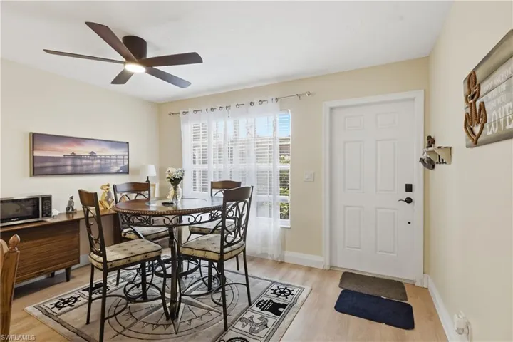 Dining area featuring wood-finish flooring, a contemporary ceiling fan with integrated lighting, and a white paneled entry door