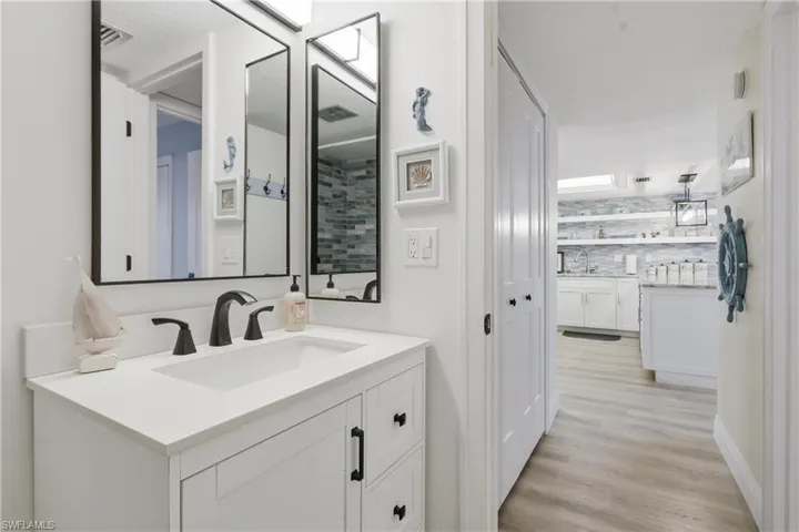 White bathroom vanity with a rectangular undermount sink and matte black faucet, illuminated by a wall-mounted light fixture
