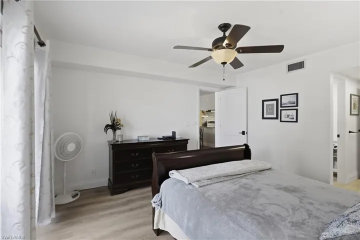 Bright bedroom featuring light wood-finish flooring, white walls, and a ceiling fan with light fixture