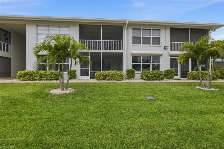 Two-story residential building featuring screened balconies and patios, white exterior walls, and multiple windows