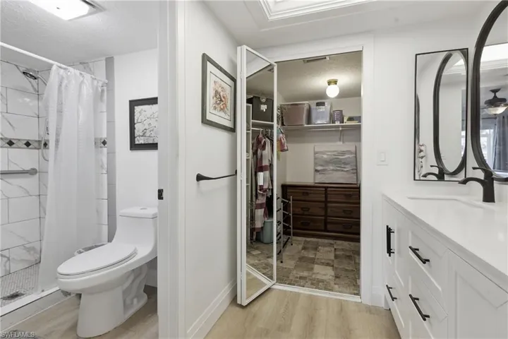 Bathroom featuring a white vanity with a rectangular sink and matte black hardware, a tiled shower with a patterned accent band, and wood-finish flooring