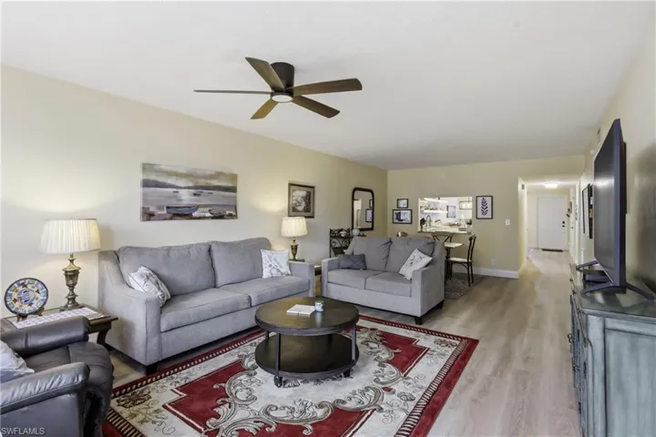 Spacious living area featuring light wood-finish flooring, a contemporary ceiling fan, and a pass-through window to the kitchen