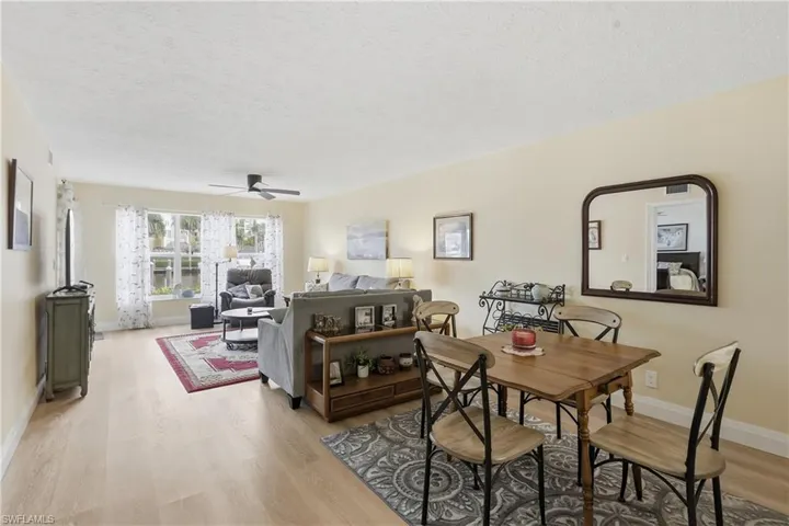 Open-concept living and dining area featuring light wood-finish flooring, a ceiling fan, and large windows with water views