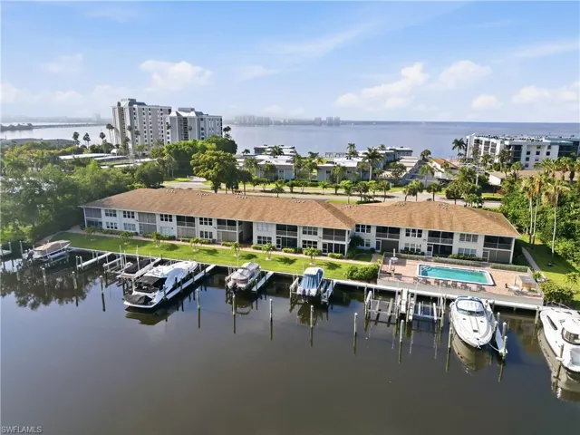 Waterfront residential complex featuring multiple boat slips, a swimming pool with a paved deck, and surrounding green spaces